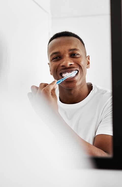 man tandenpoetsen in spiegel met Colgate-tandenborstel